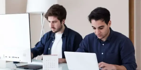 Deux hommes travaillant côte à côte devant des ordinateurs.
