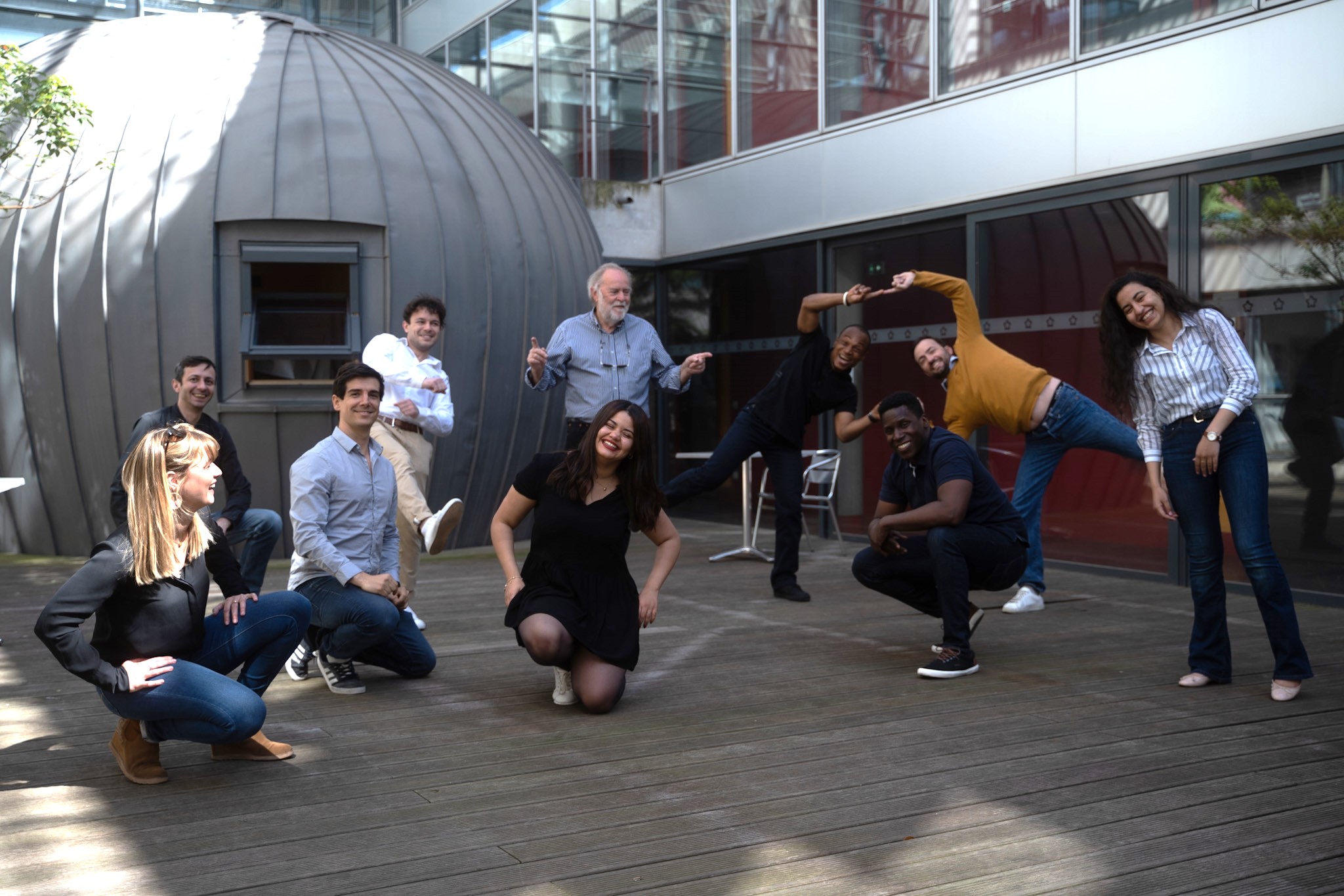 Photo de l'équipe de 10 salariés à l'extérieur du bâtiment. Ils prennent des poses amusantes et différentes.