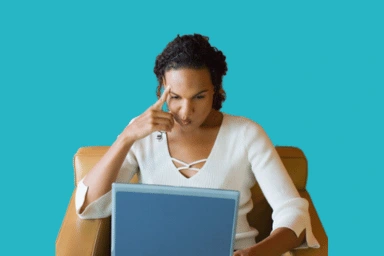 Woman sitting looking at a laptop, her face expresses a feeling of doubt and indecision.